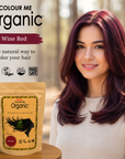 Woman with wine red hair next to 'Colour Me Organic' hair color packaging in a forest setting