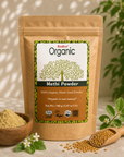 A stand-up kraft pouch of Radico Organic Methi Powder is shown on a light neutral surface with a bowl of loose powder, a wooden scoop of seeds, and green plant leaves in the background.