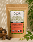 A stand-up pouch of Radico Organic Reetha Powder hair wash and treatment, displayed on a beige surface with a small wooden bowl of dried reetha pods, green leaves, and soft shadow lighting in the background.