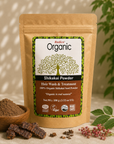 A stand-up pouch of Radico Organic Shikakai Powder hair wash and treatment, shown with a bowl of loose powder, dried shikakai pods, and green leaves on a neutral surface.