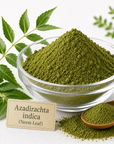 Green neem powder piled in a clear glass bowl, with a small wooden spoon of powder, scattered powder, and a label reading 'Azadirachta indica (Neem Leaf)' on a white background with green neem leaves.