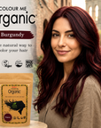 Woman with burgundy hair next to 'Colour Me Organic' hair color packaging with a cityscape background.