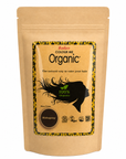 A stand-up kraft paper pouch of Radix Organics 'Colour Me Organic' hair color in the shade 'Mahogany'. The packaging features a central label with a black silhouette of a flowing hair profile, a circular brown color swatch, and a yellow and black patterned border.